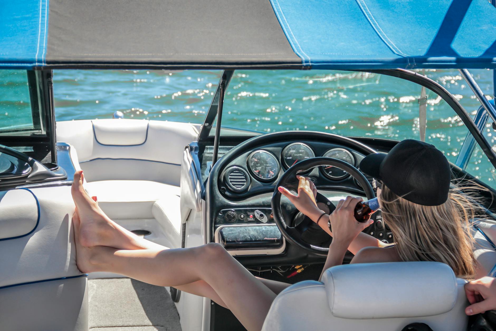 High-Net-Worth Individuals woman wearing black cap holding bottle on white speedboat during daytime