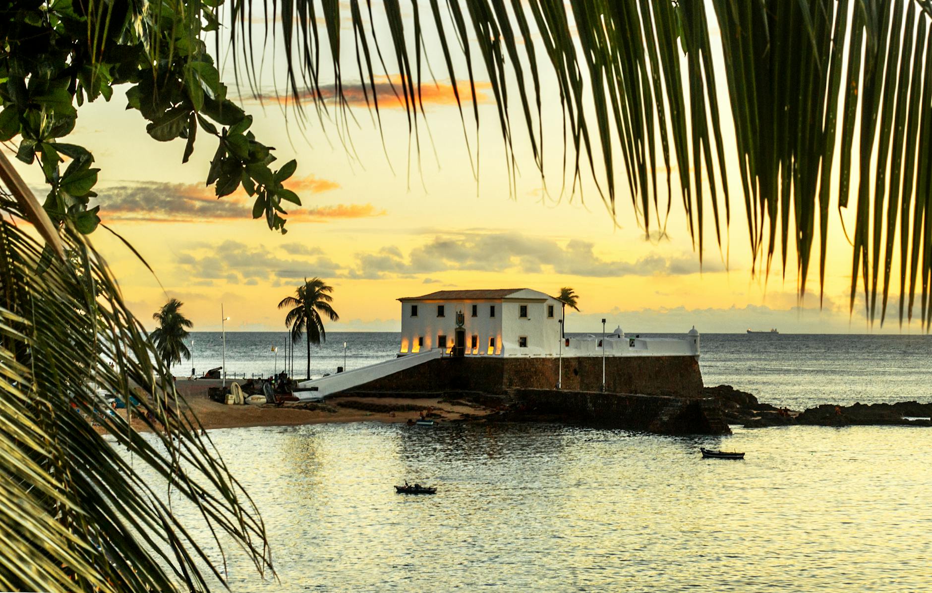 white illuminated house on the sea and palm leaves in foreground
